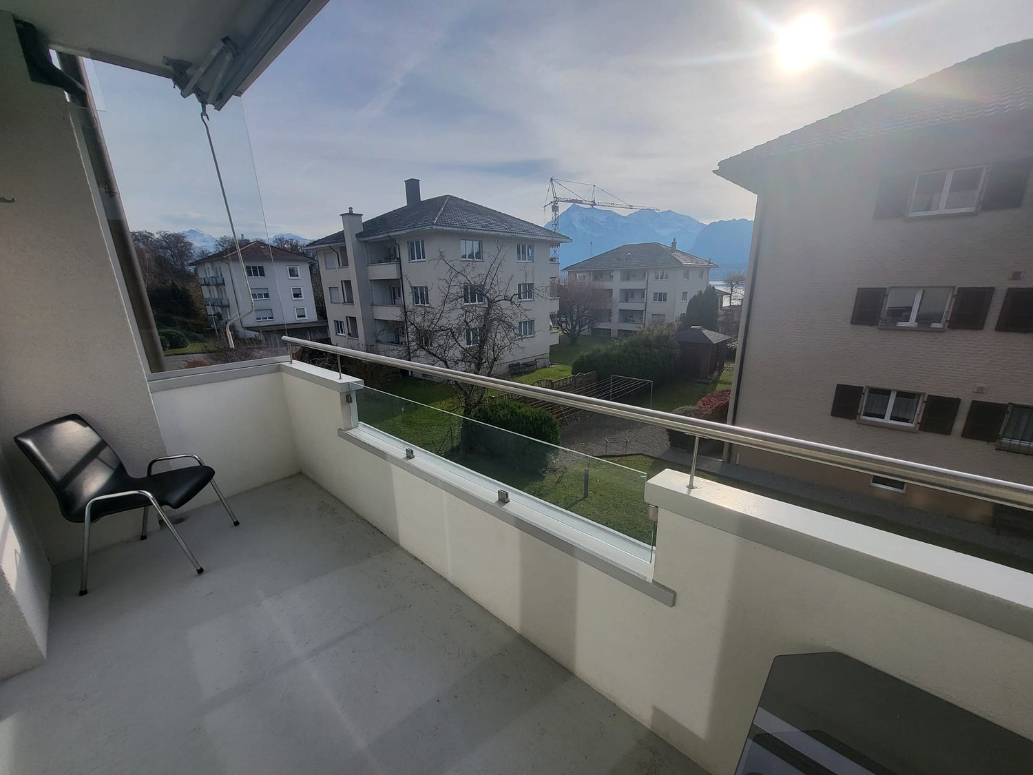 Modern balcony with glass railing, floor and wall, a black chair, city view