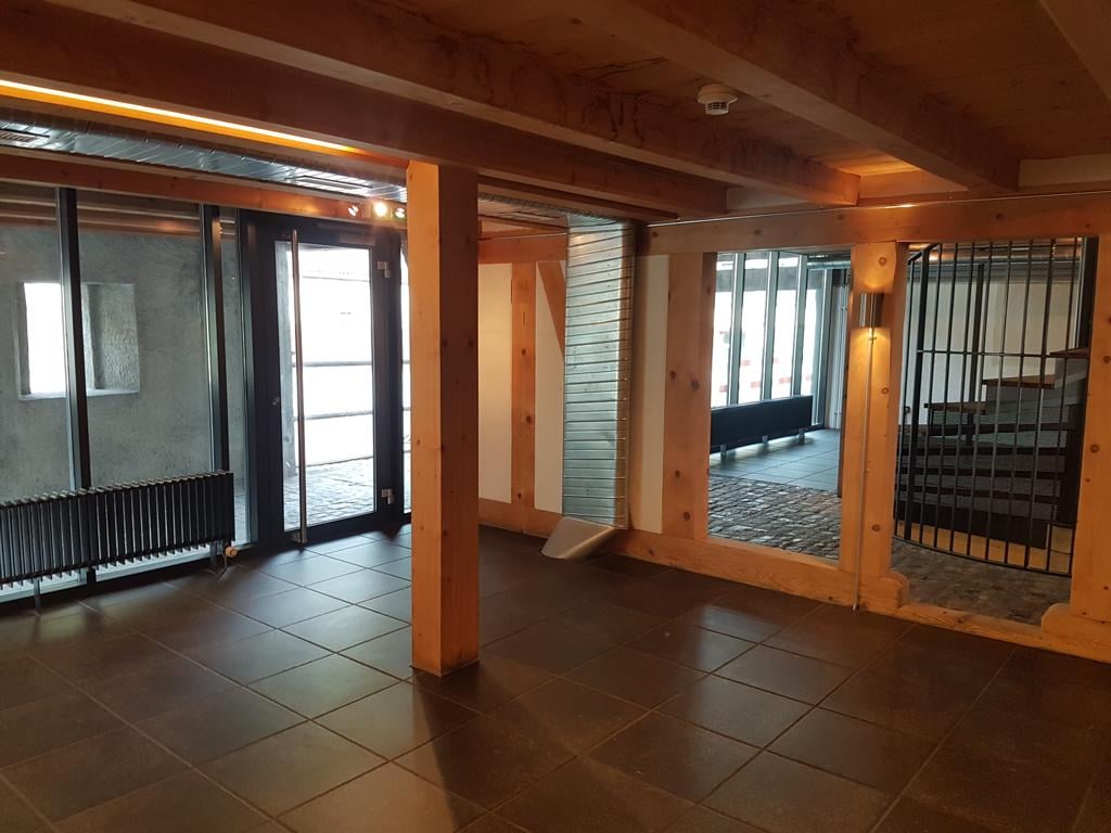 Empty room with wooden beams, tiled floor, glass doors, radiator, surveillance camera