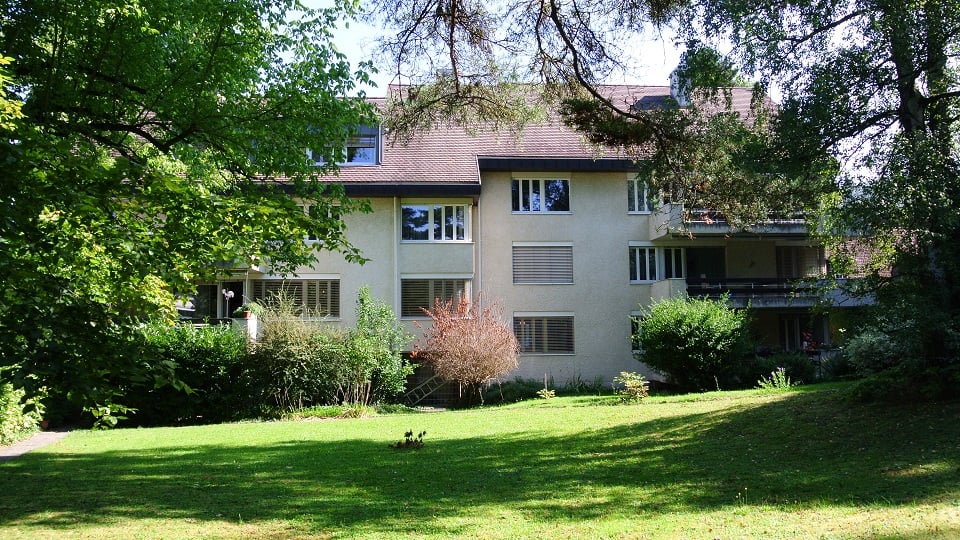 2 story house, beige exterior, 4 balconies, surrounded by trees and greenery