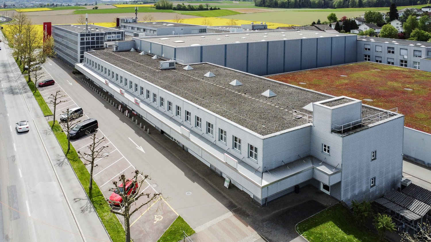Large industrial building, white paint, flat roof, windows, parking spaces, road