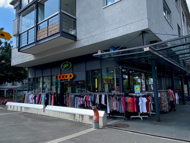 Large building with glass facade, clothing store, metal awning, rack with clothes