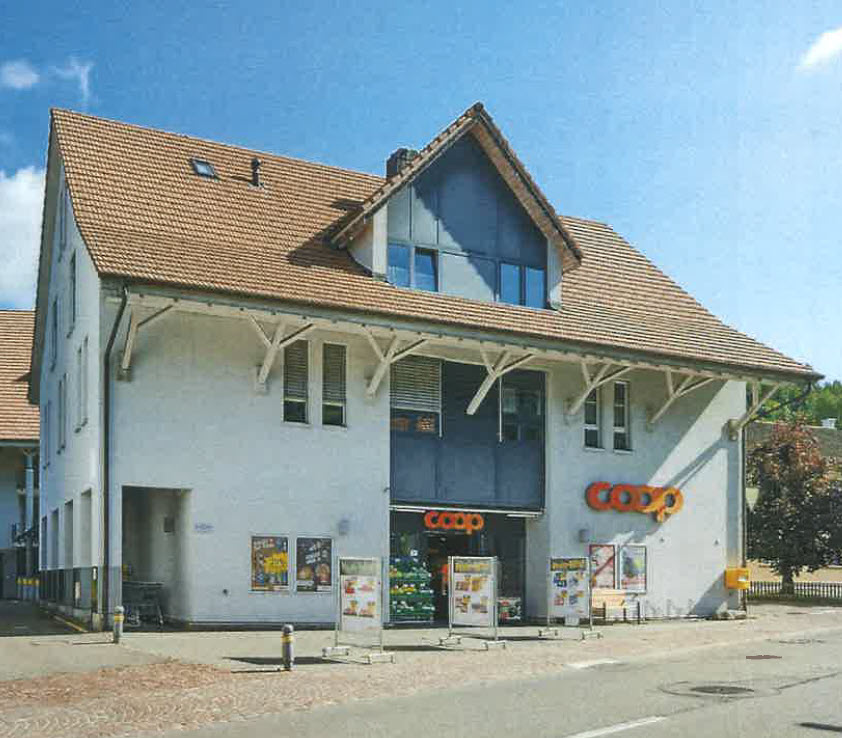 Two story building with brown roof, blue windows, entrance door, sign reads 'COOP', trees and street in front