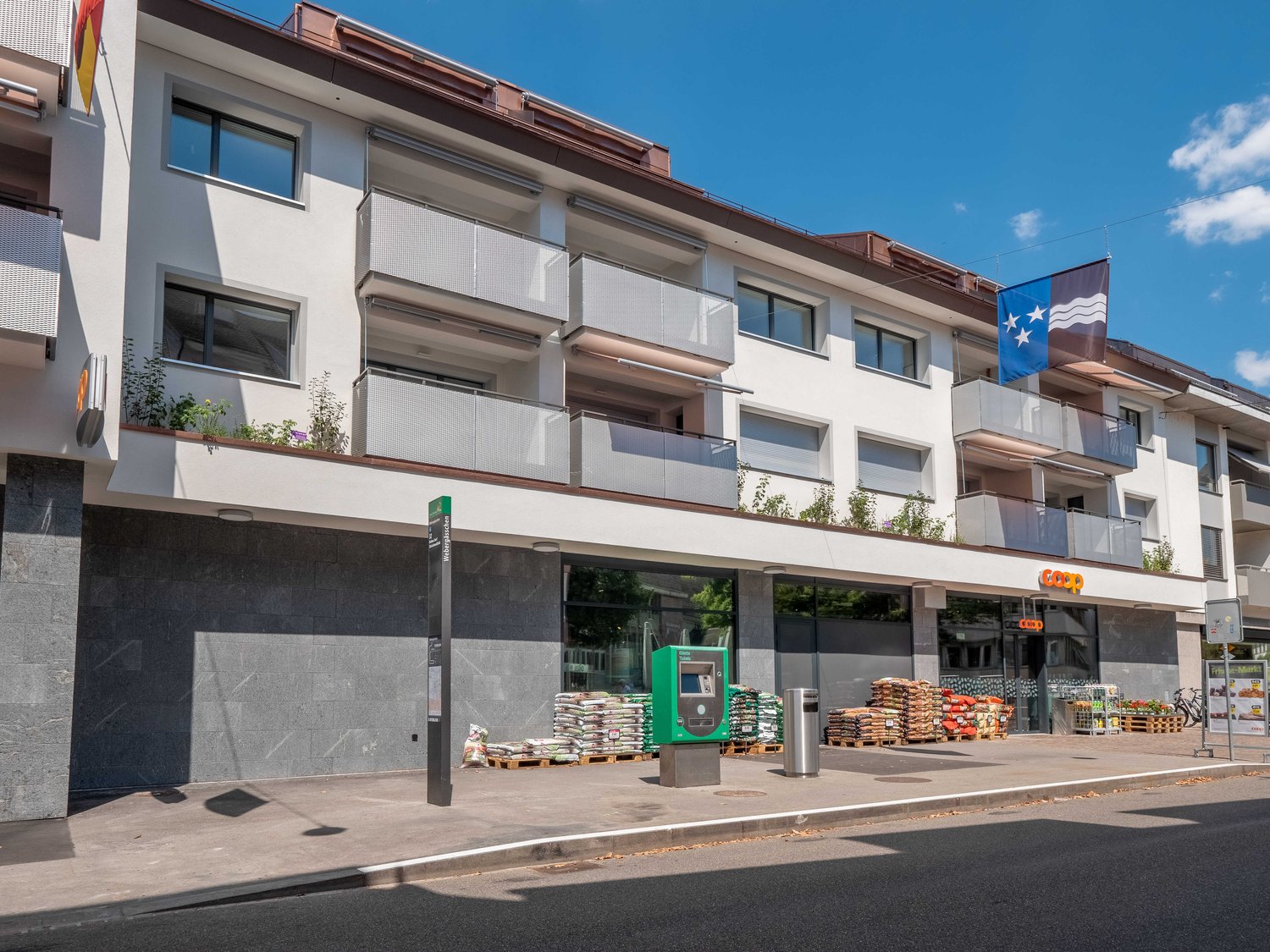 3-story apartment building with white exterior, balconies, and a retail store on the ground floor