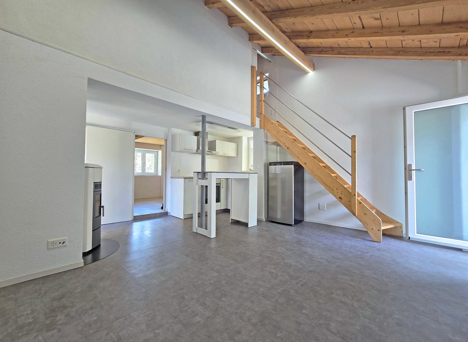 open floor plan, wooden ceiling, white walls, gray floor, kitchen, staircase, refrigerator, fireplace