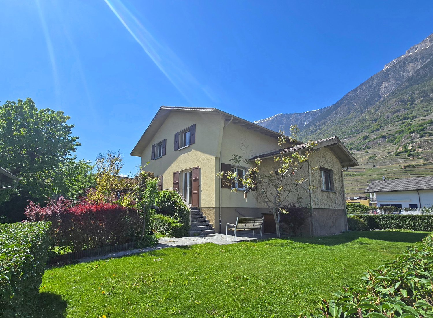 2 story house, yellow exterior, brown shutters, mountain view, garden, bench