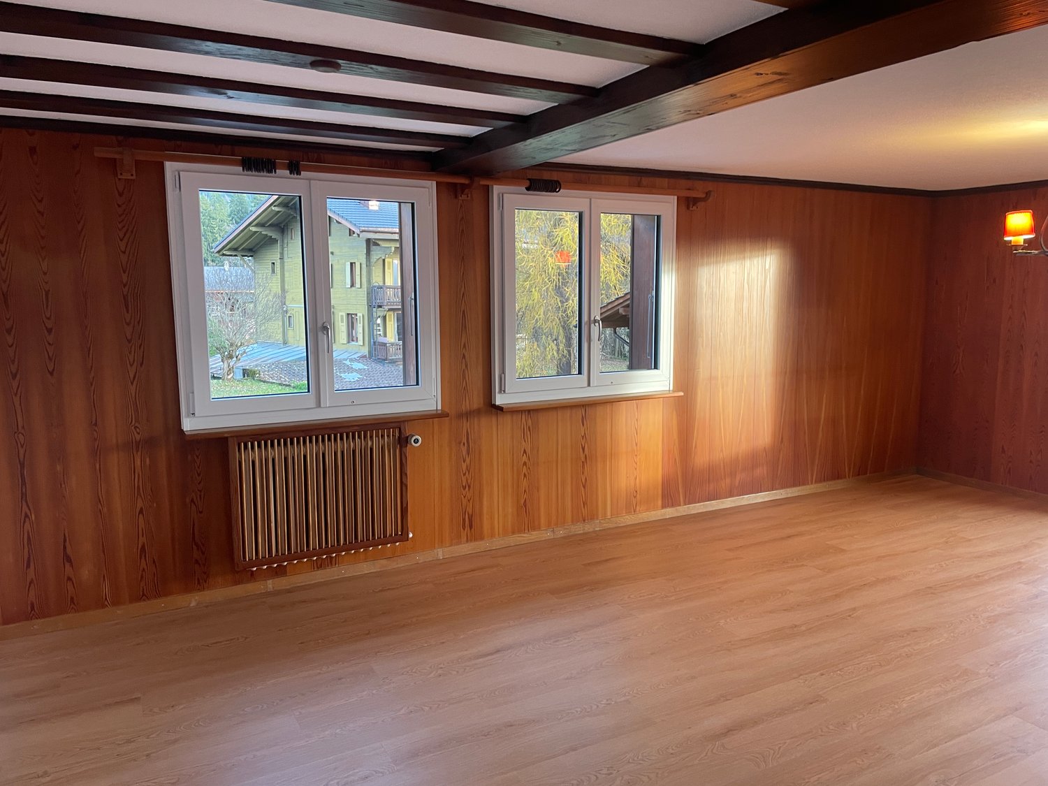 empty room, wooden walls, two windows, wooden floor, white ceiling, radiator, lamp