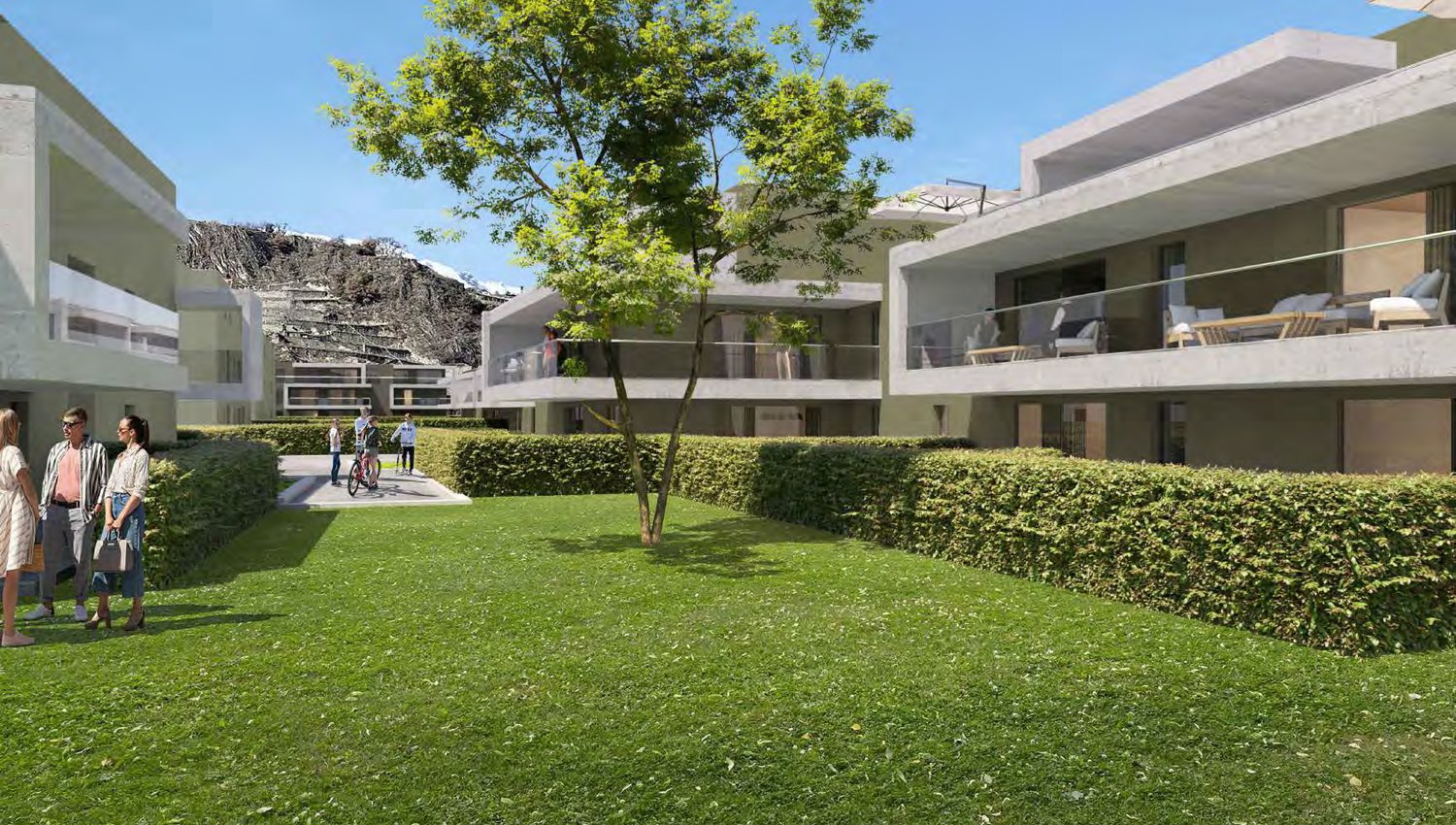 The image shows a modern apartment complex with a central courtyard area. The buildings have a minimalist, contemporary design with large windows and balconies. The courtyard is well-landscaped with a grassy lawn, hedges, and a tree in the center. There a