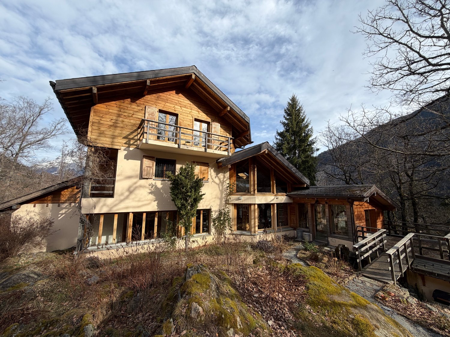 two-storey chalet made of wood, multiple balconies, panoramic windows, located on the hillside with forest and mountain view