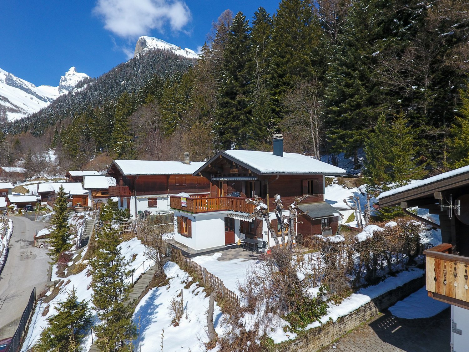 chalet style house, wooden exterior, snow covered roof, balcony, surrounded by trees and mountains