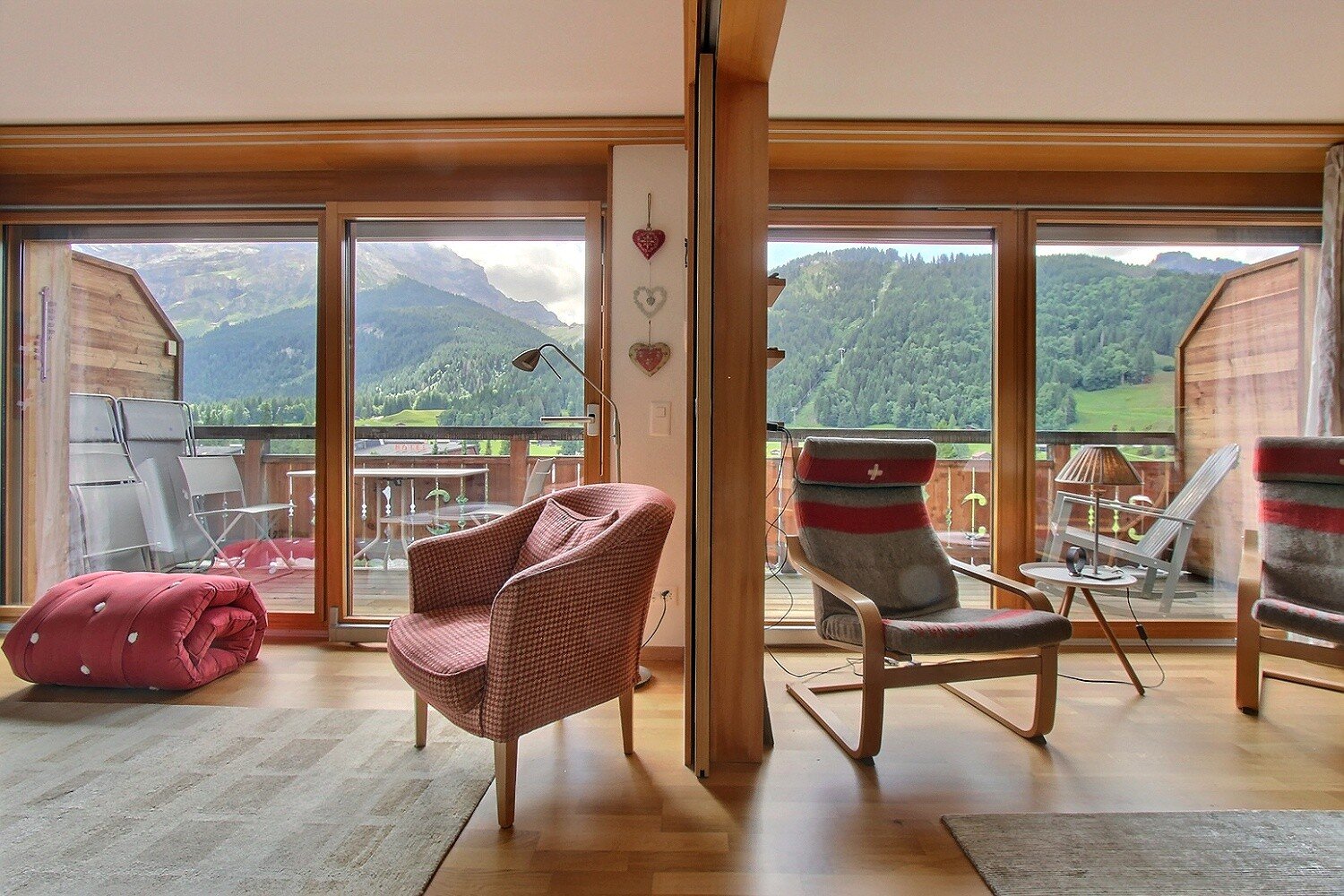 living room, wooden floor, beige walls, sliding glass doors, chairs, cushions, outdoor table, balcony, glass railings, lamps, decorative items, carpet, mountain view