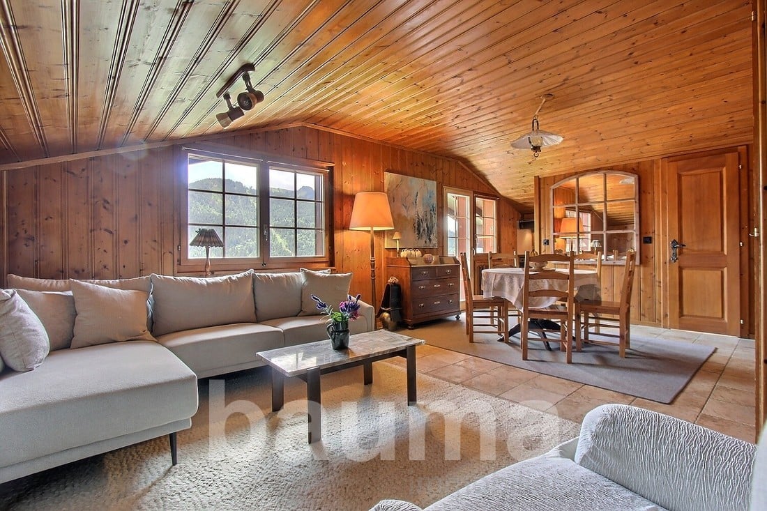 Spacious living room with wooden walls and ceiling, large windows, comfortable sofa, coffee table, and a fireplace