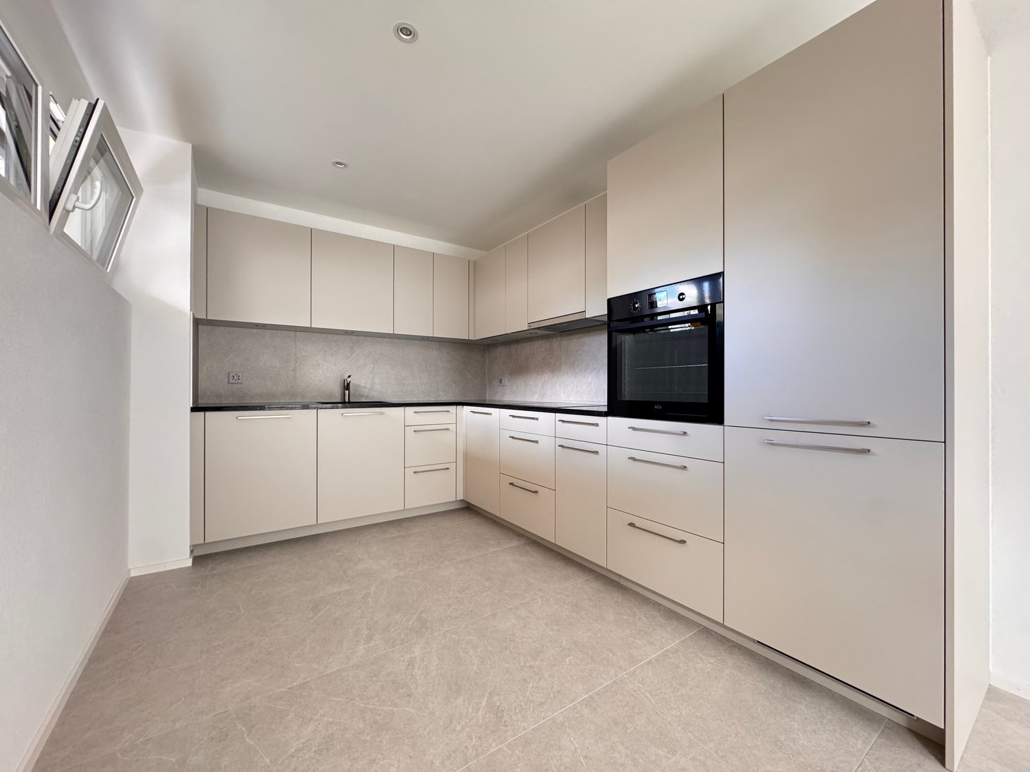 a modern, minimalist kitchen with sleek, neutral-colored cabinets, black countertop, black oven, and neutral-toned flooring.