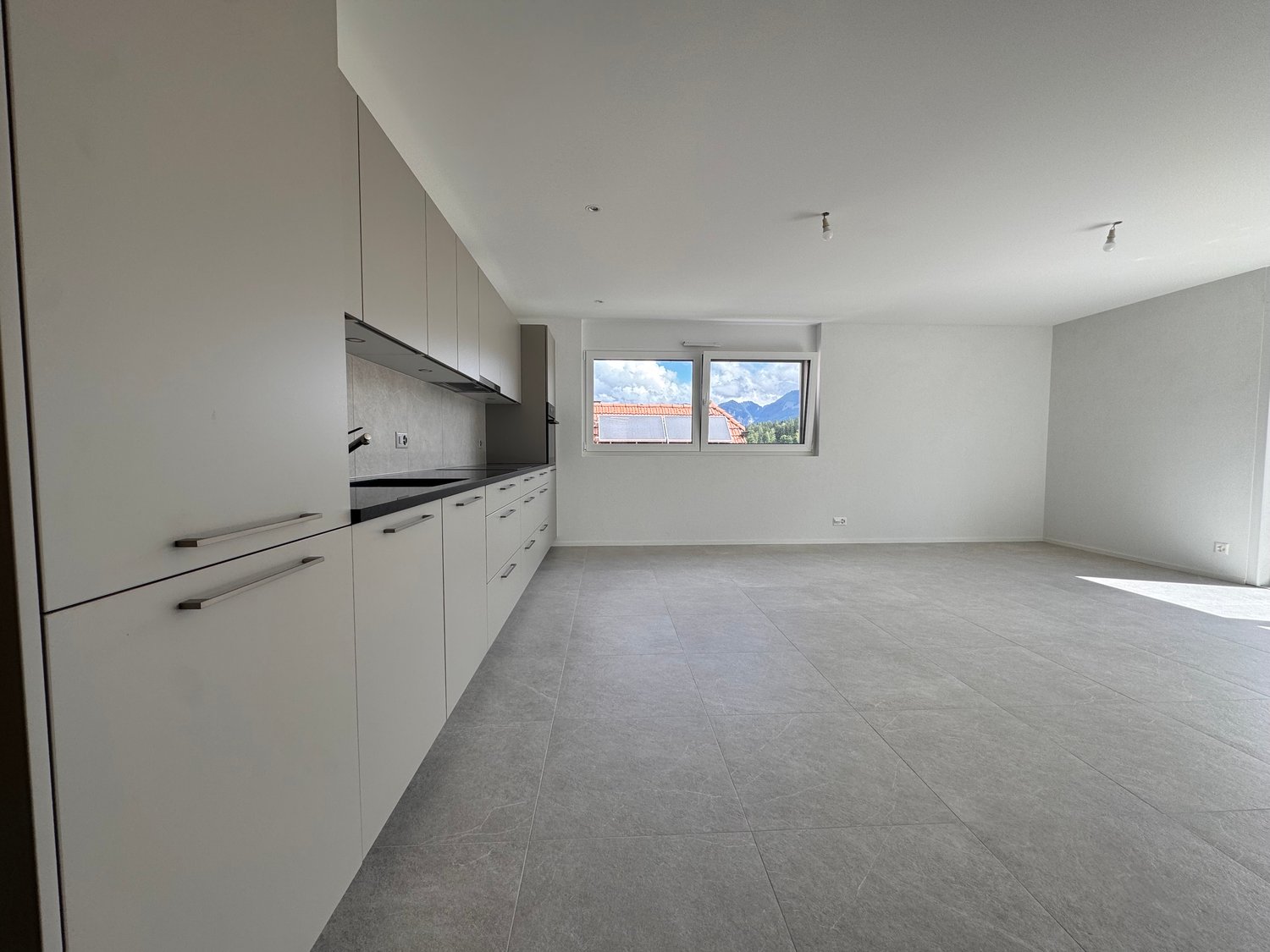 Modern kitchen with white cabinets, tiled floor, black countertops, large window, and power outlets.