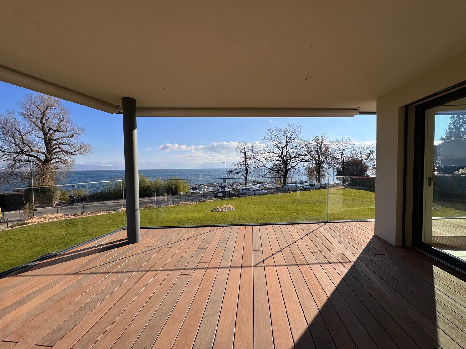Balcony with wooden floor, glass railing, unobstructed sea view, well-maintained lawn