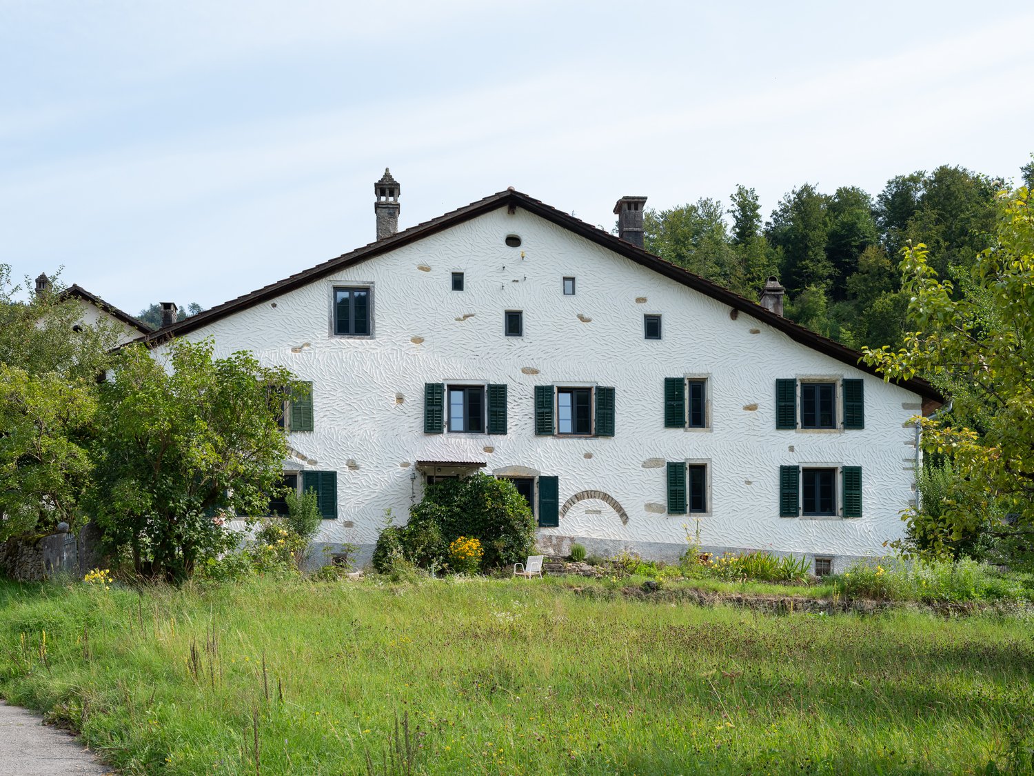 Two-story house, white exterior, green shutters, two chimneys, surrounded by trees and grass