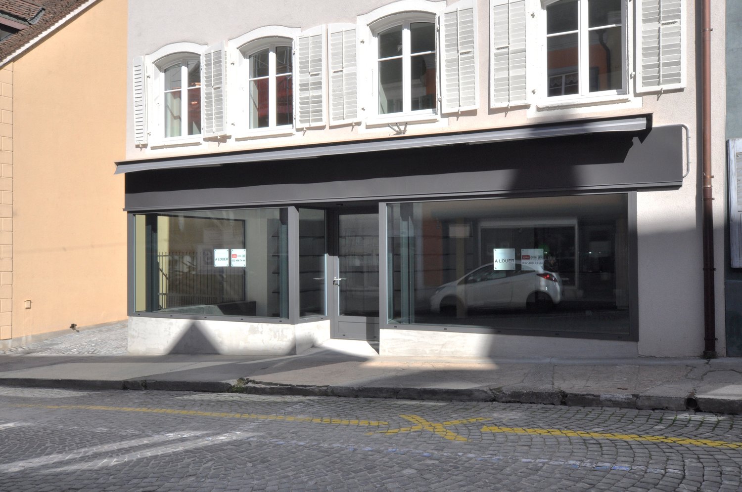 Storefront with glass windows, white shutters, black awning, white car visible inside