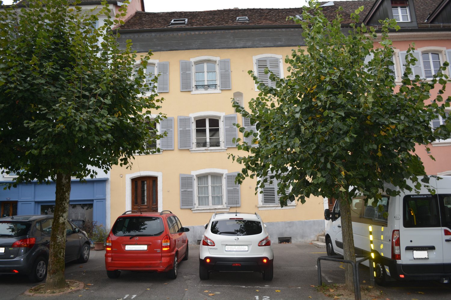 3 story yellow building, grey shutters, double doors, multiple windows, parked cars, visible parking spots