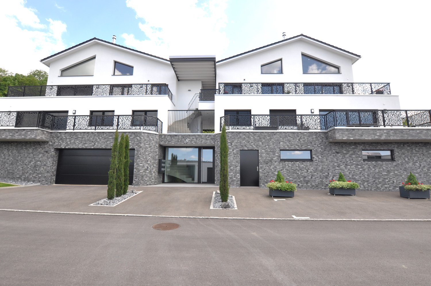 2 story modern house, white and grey exterior, two garages, balconies on each floor, planted area in front