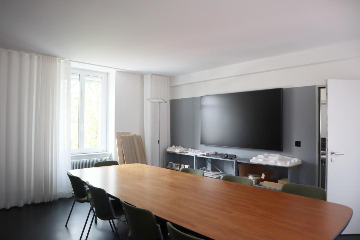 conference room, long wooden table, chairs, mounted TV, curtains, window, floor lamp