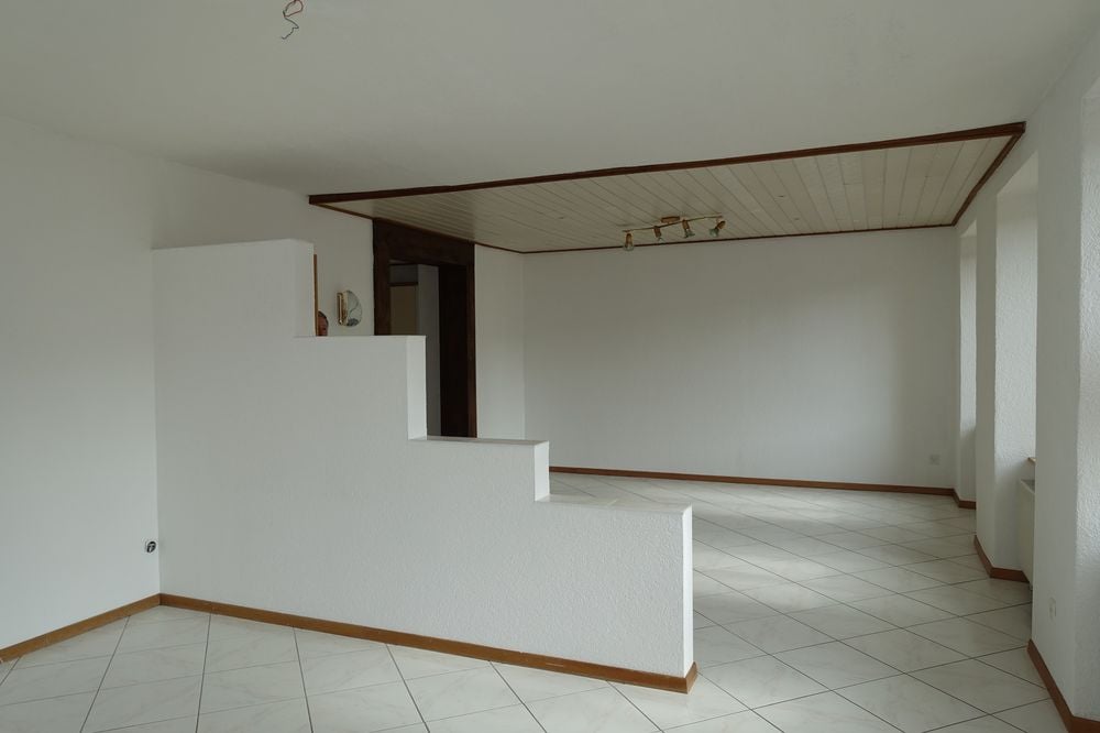 Empty room with white walls, white tiled floor, wooden trim, and a ceiling with lights.