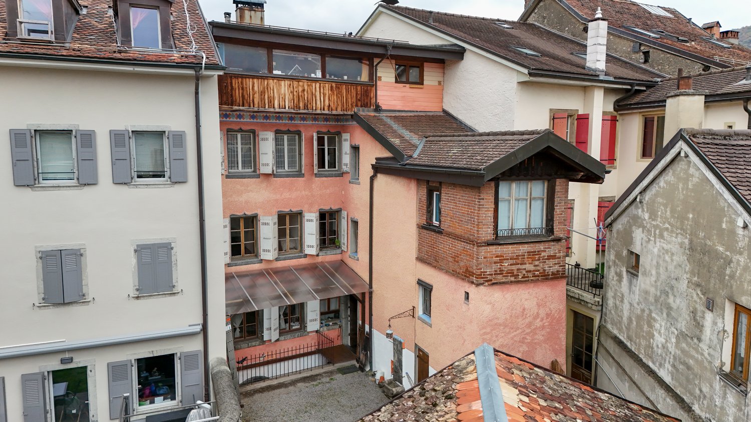 Multiple buildings with balconies, brick and wood construction, various window sizes, red shutters