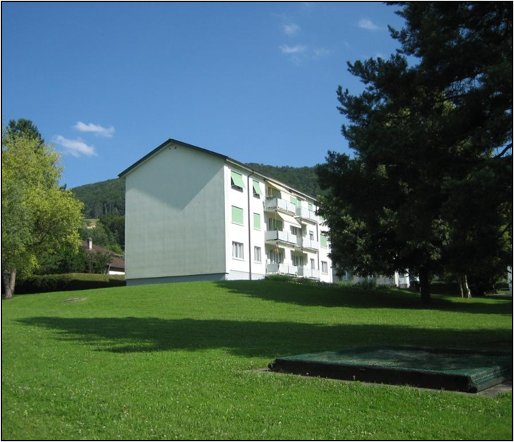 3-story apartment building with green exterior, surrounded by a grassy lawn and trees