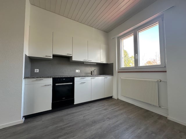 white cabinets, gray countertops, black oven, large window, white radiator