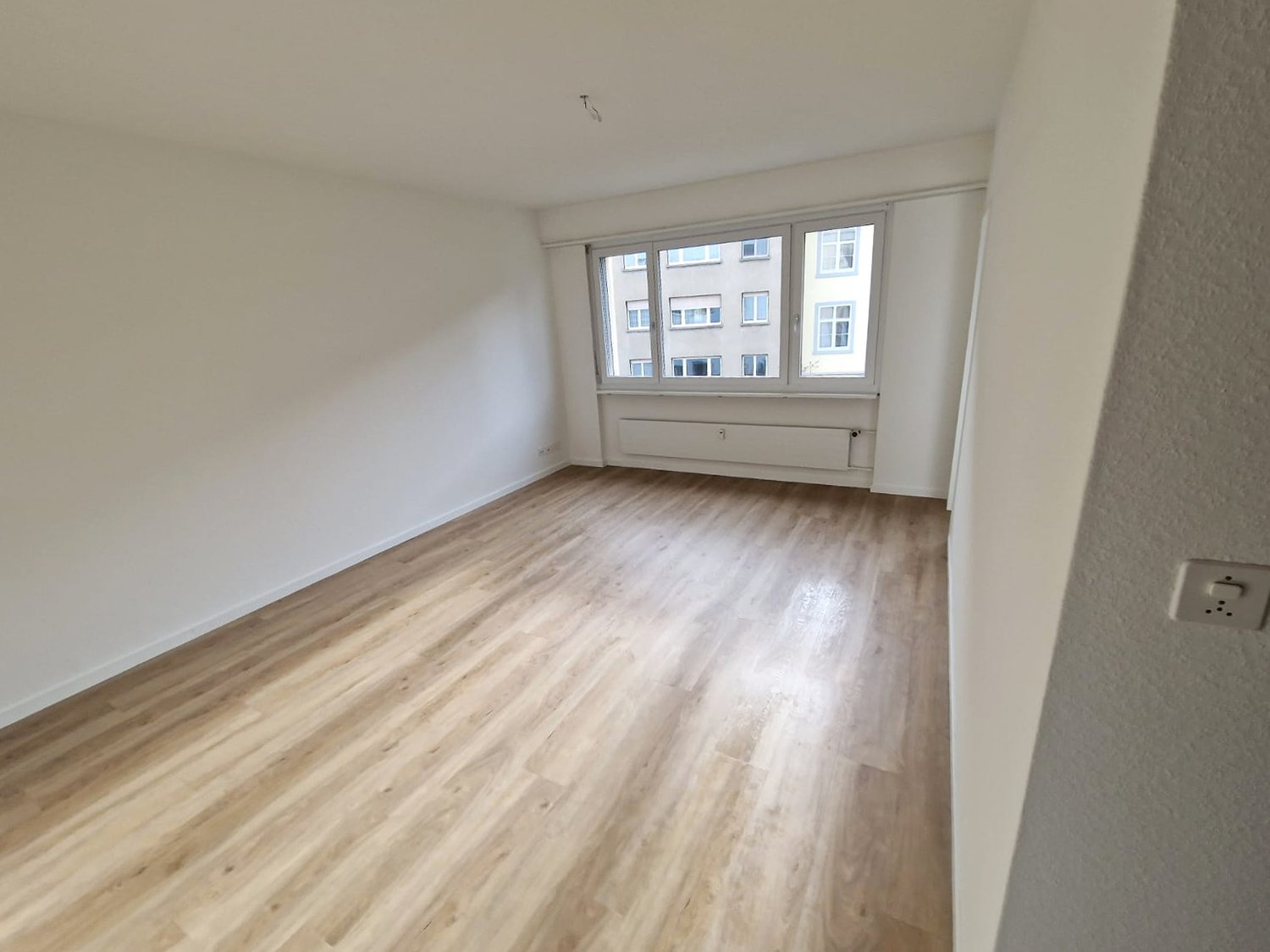 empty room with wooden floor, large window with view, white walls, white ceiling