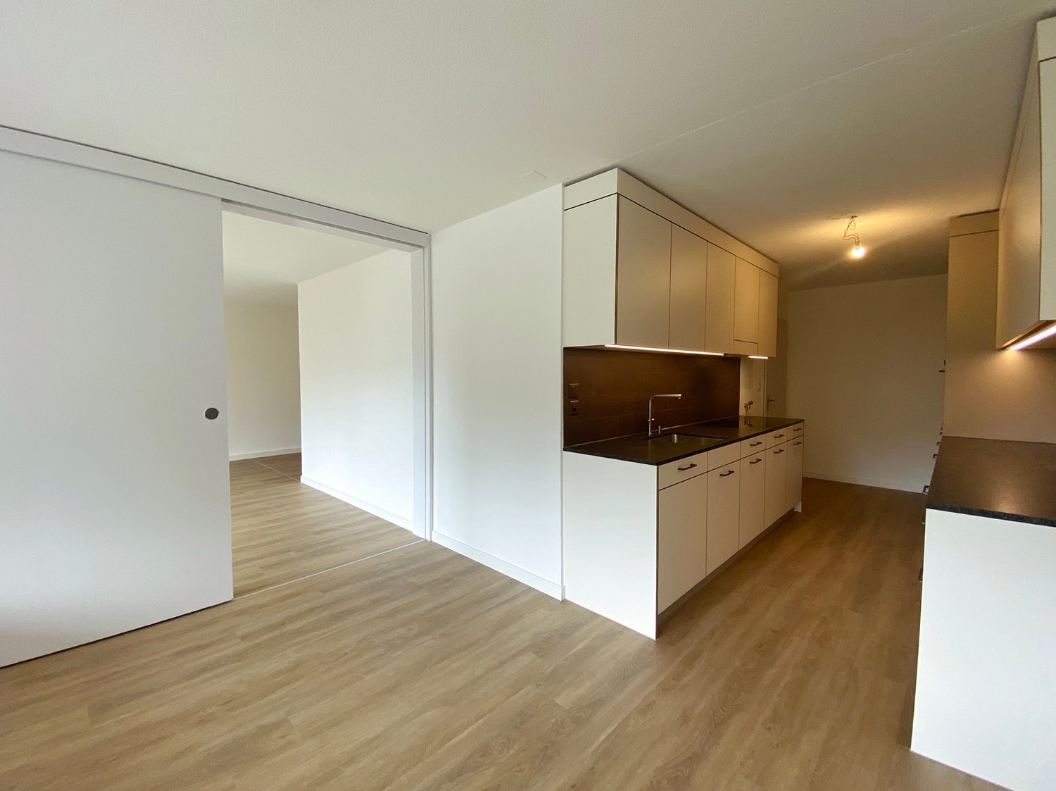 kitchen with black countertops, white cabinets, open door, light wooden floor