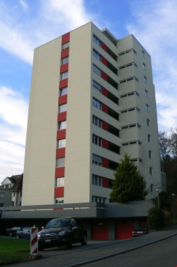 high building with red vertical lines, multiple windows, car parked in front, garage, other cars parked in the distance