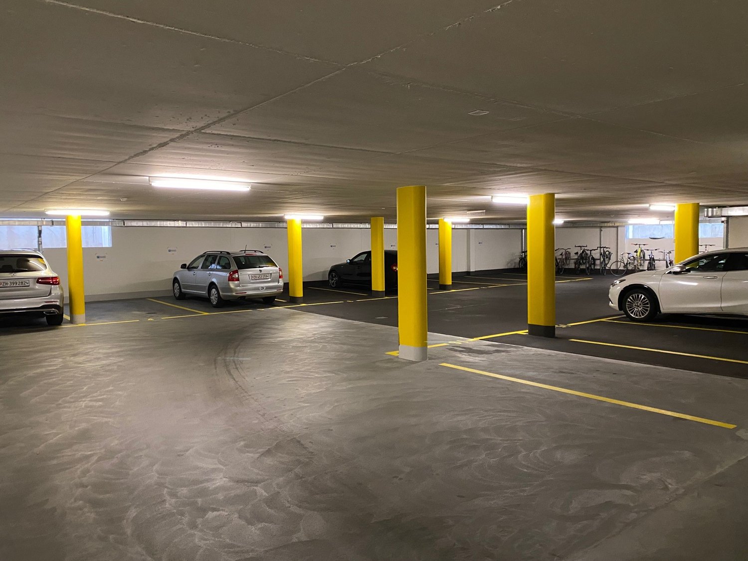 underground parking lot with yellow pillars, 4 cars parked, bicycles parked on the side