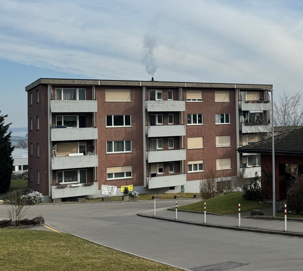 A multi-story residential building with balconies and a smoke stack on the roof.