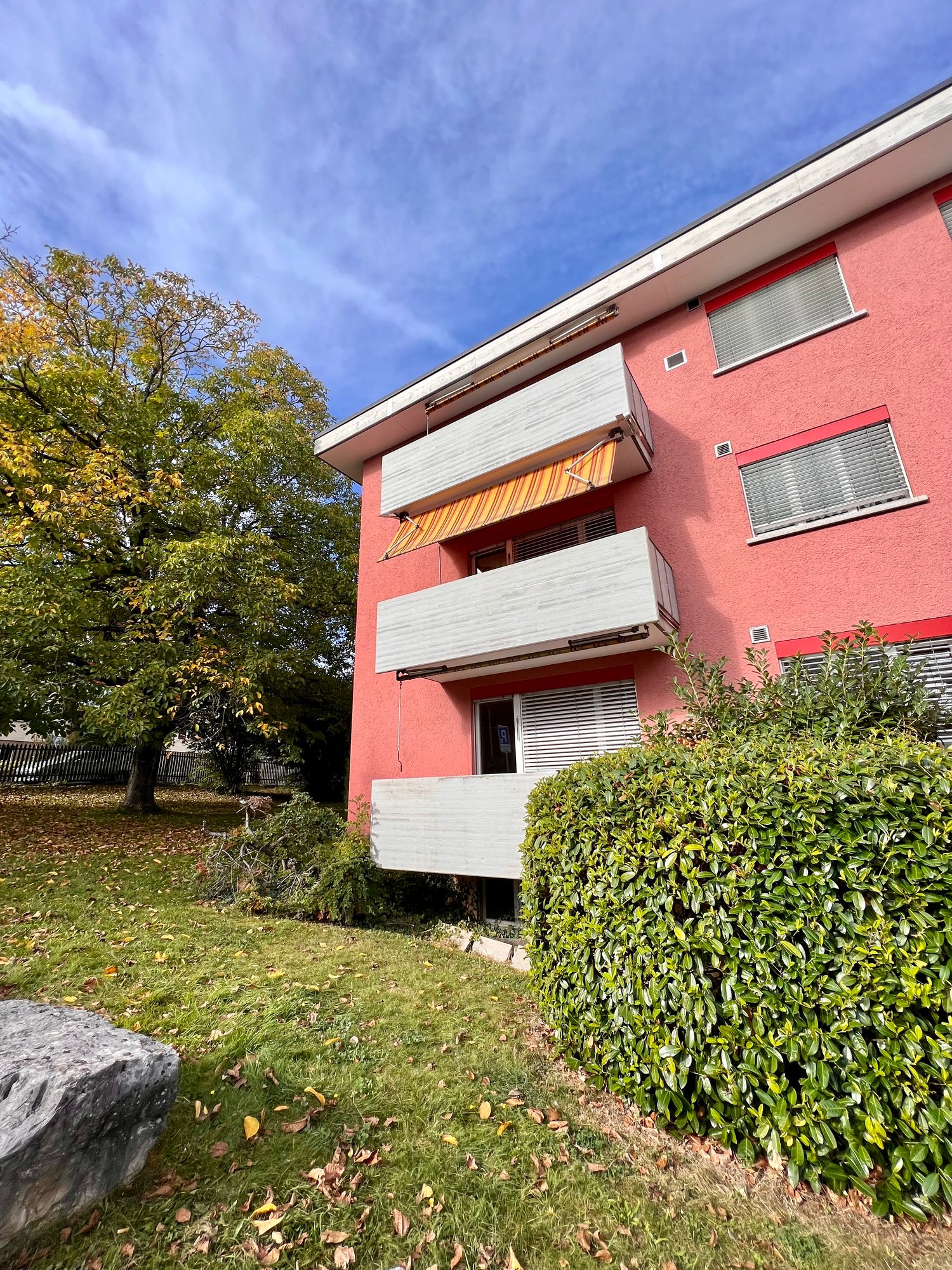 Red building with balconies, multiple windows, exterior wall with white brick and window vents, concrete pathway