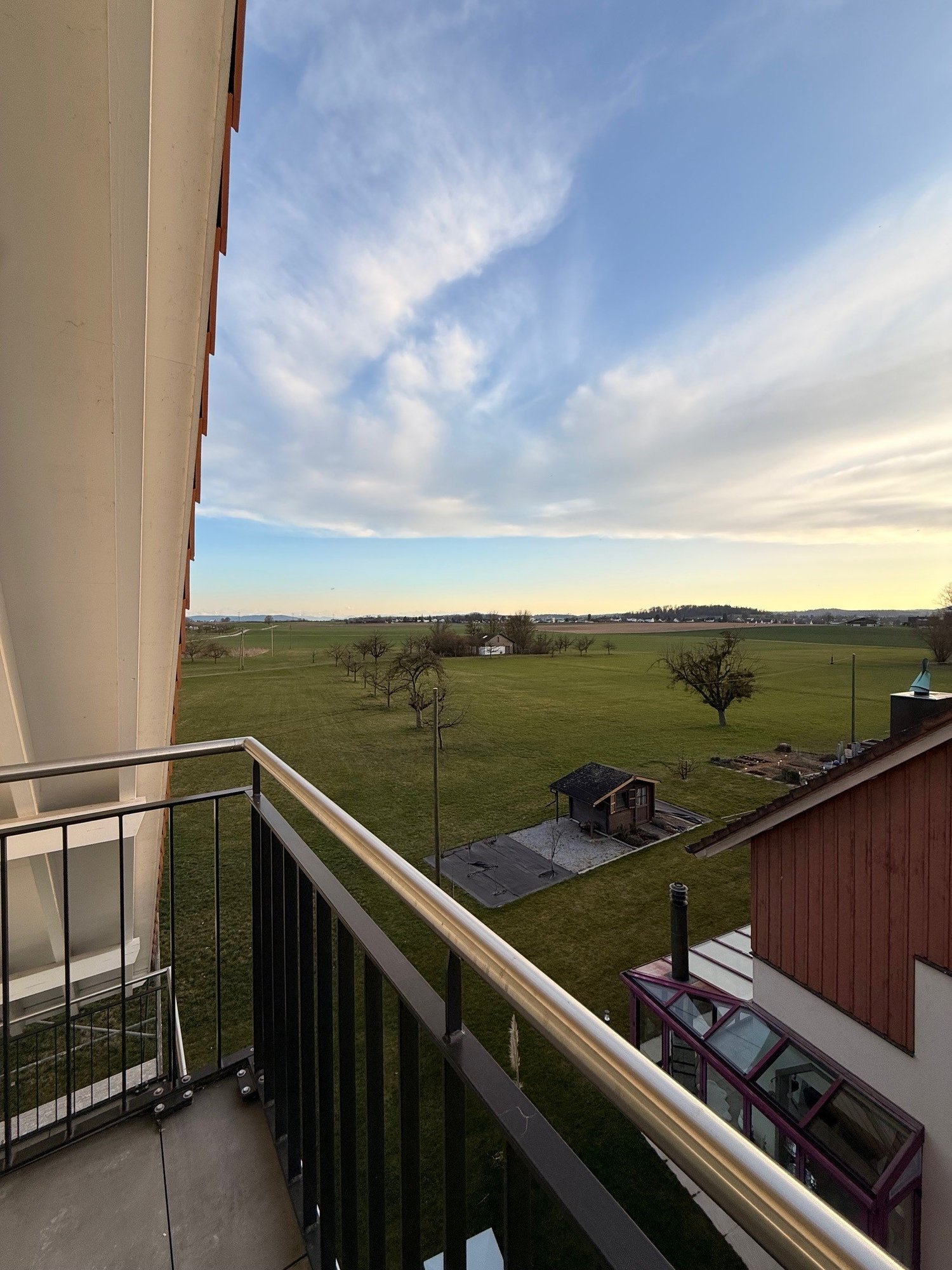balcony with railing, green field, distant house, small shed, clear sky, metal railing