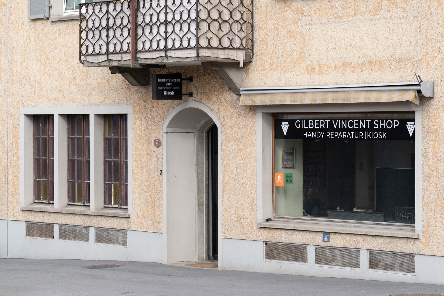 2-storey building with an arched entrance, brown wooden balcony, white awning, Gilbert Vincent shop at ground floor, and several windows