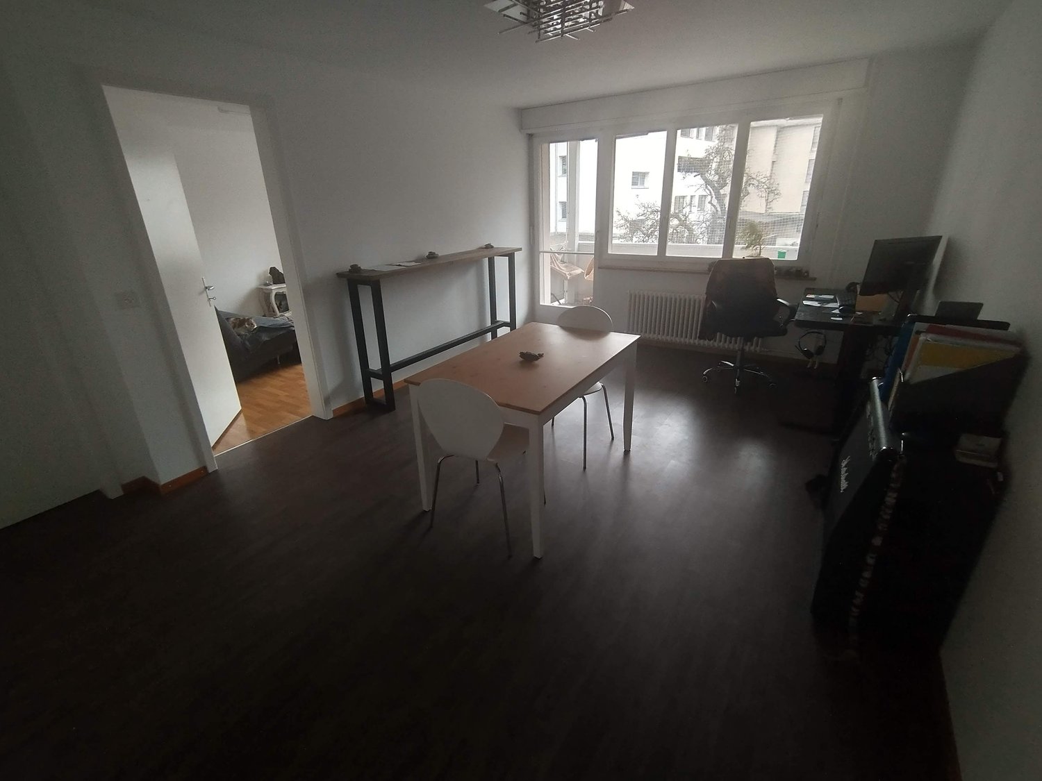 bright room with wooden floor, a table, chairs, a long desk, office chair, desk, monitor, radiator, large windows, door