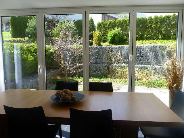 Large dining table with black chairs, overlooking a lush garden through floor-to-ceiling windows