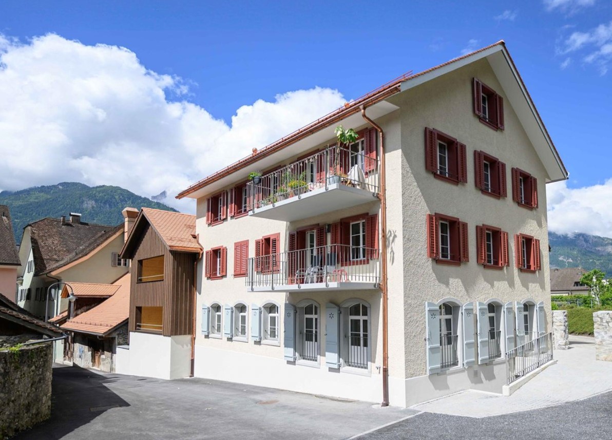 3 story white house, red shutters, brown roof, red shutters balconies, street view, mountains in background