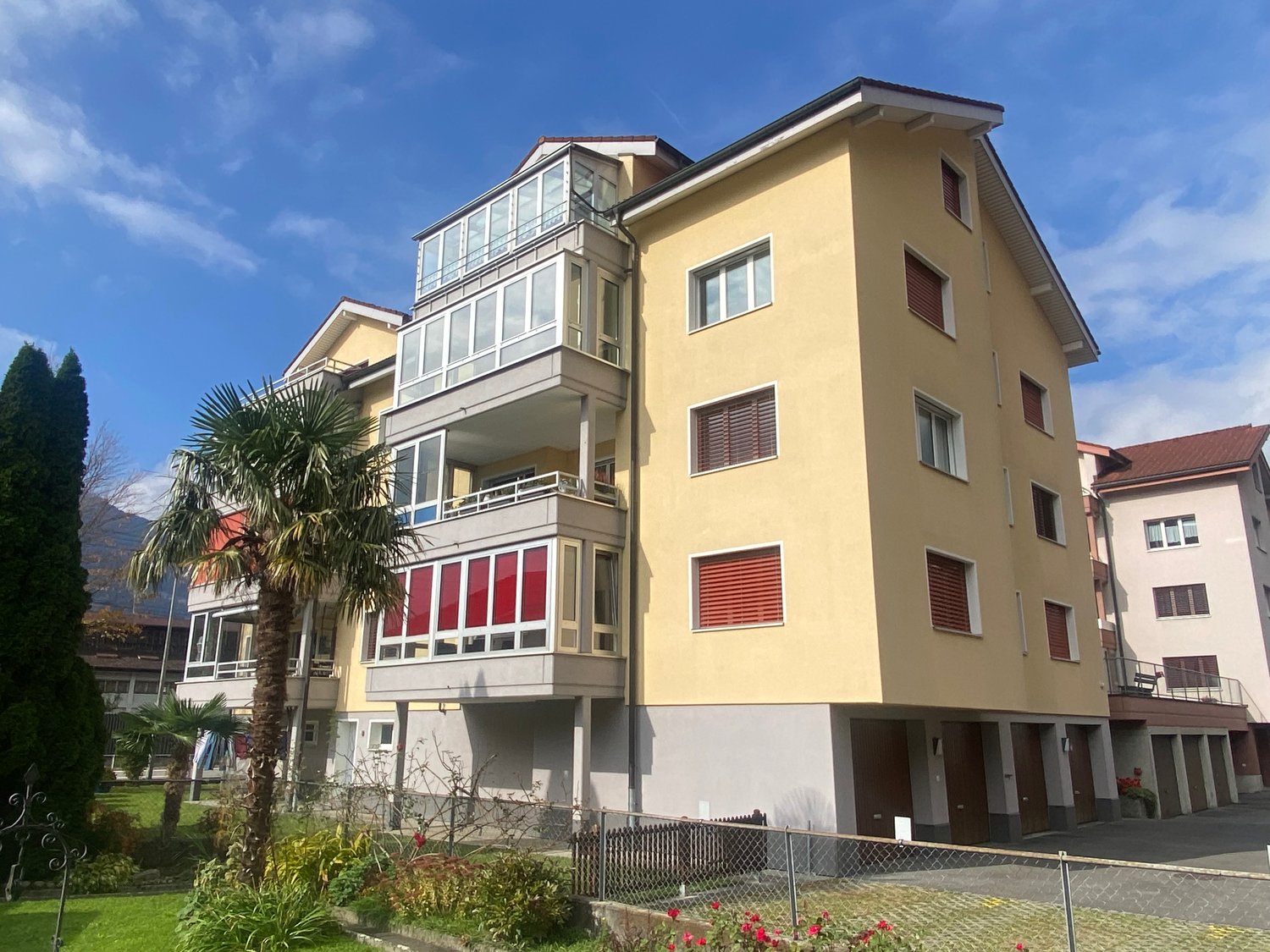 5-story apartment building, yellow exterior, multiple balconies, gated entrance, red-framed windows, red roof