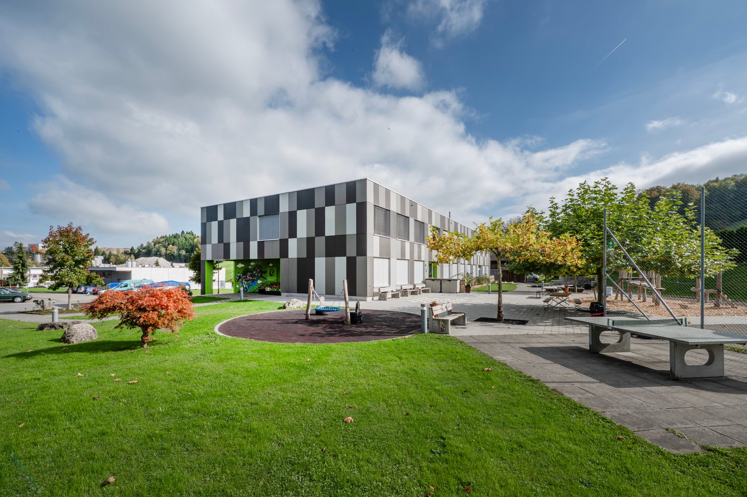 Contemporary architectural building, checkerboard pattern facade, children's playground, trees, bench, table tennis
