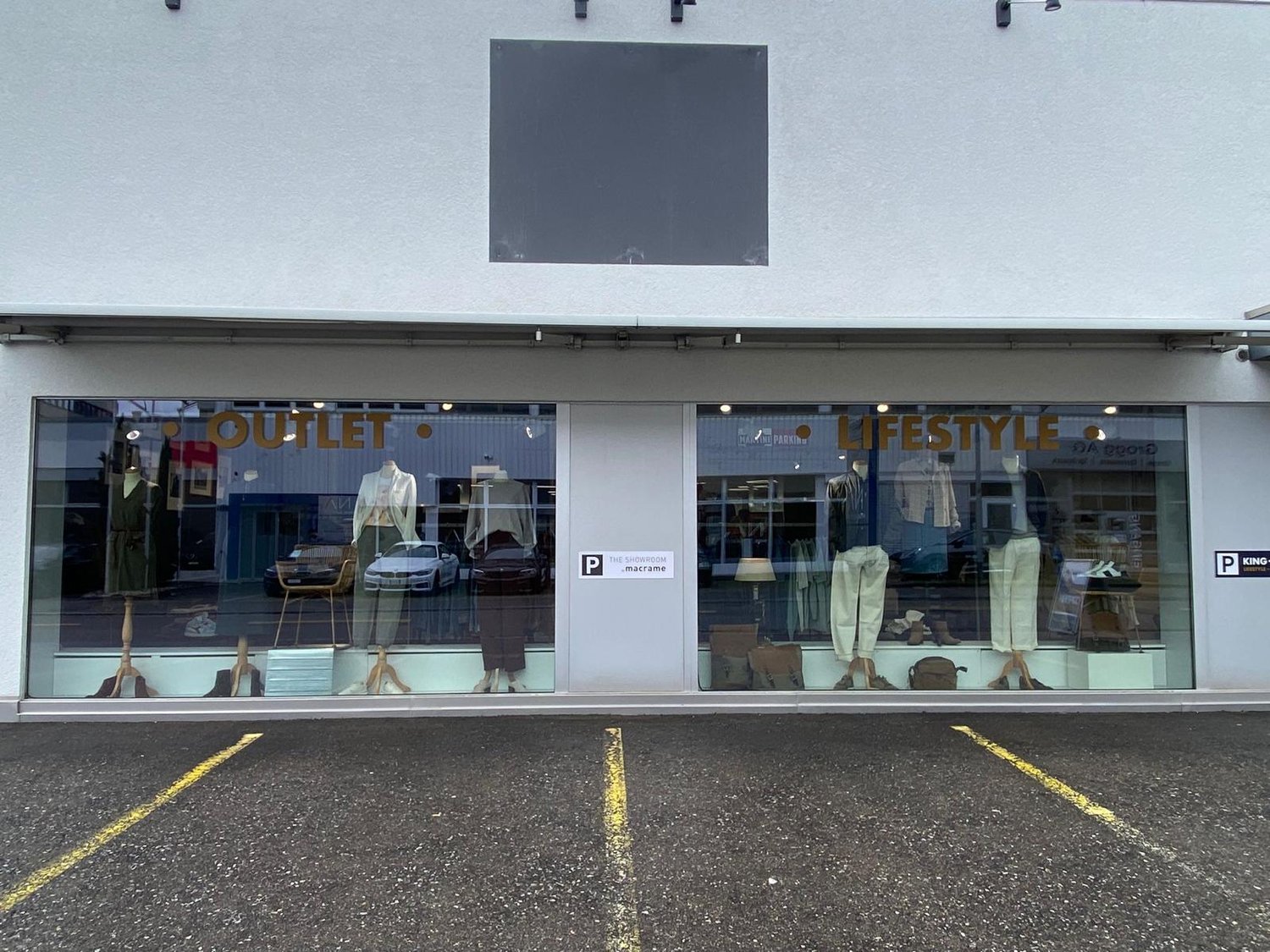 Storefront with glass windows and parking area in front, mannequins and displayed clothes inside
