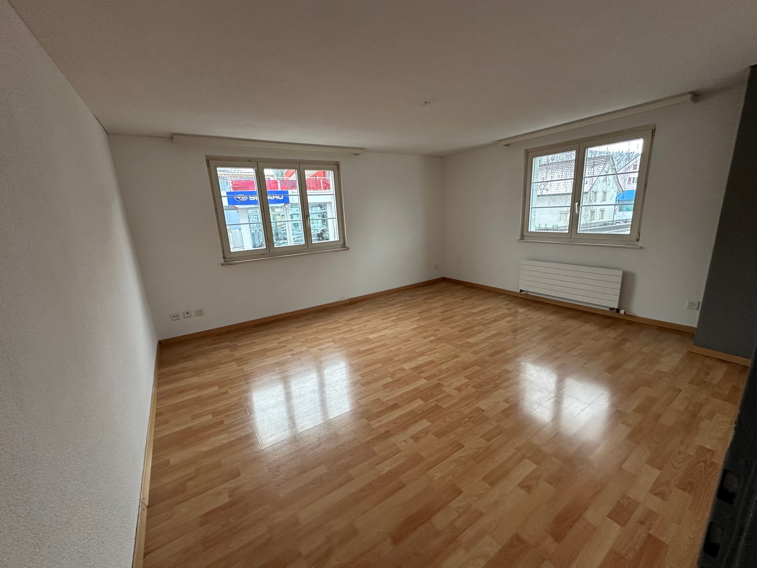 Spacious room with hardwood flooring, large windows, and a radiator. The room appears to be empty, ready for furnishing and occupancy.