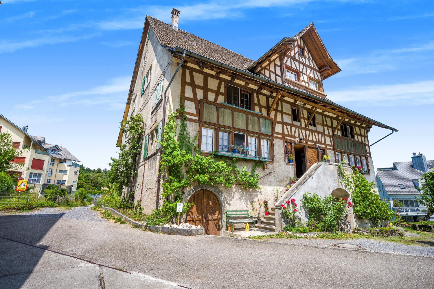 2 story traditional house, brown wooden walls, large windows, brick roof, brown wooden door, stairs with plants and flowers, bicycle near the stairs