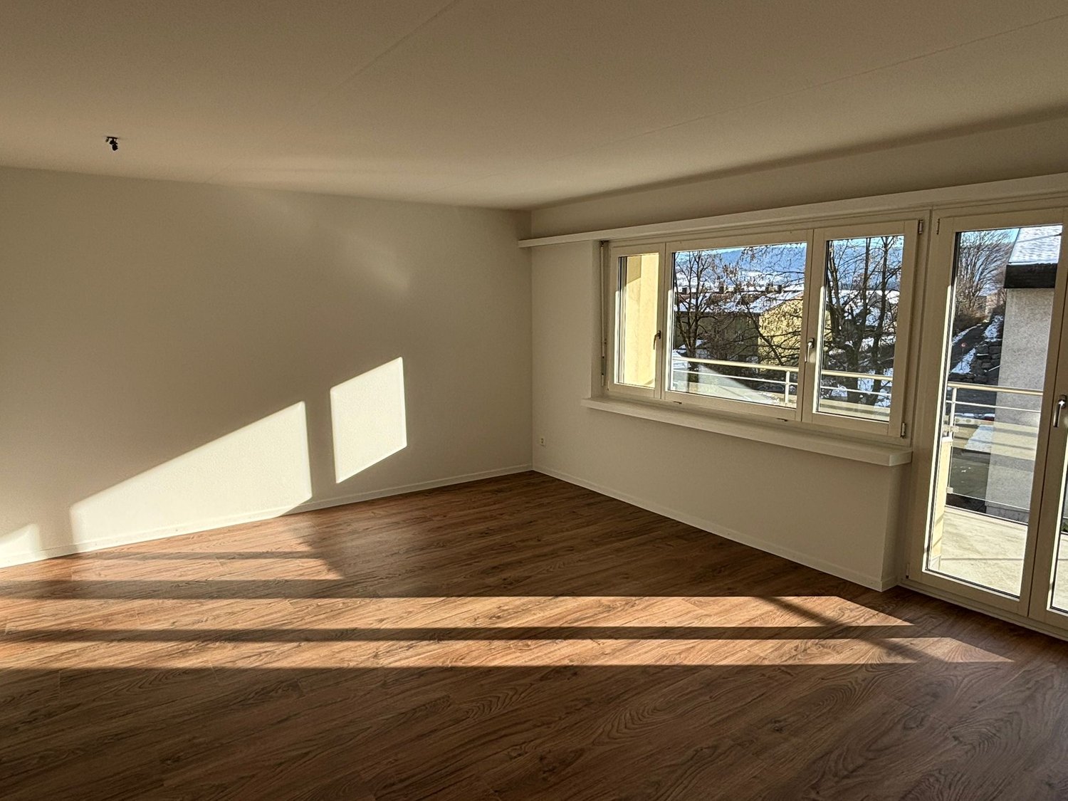 Empty room, wooden floor, white walls, sliding glass doors to balcony, double window