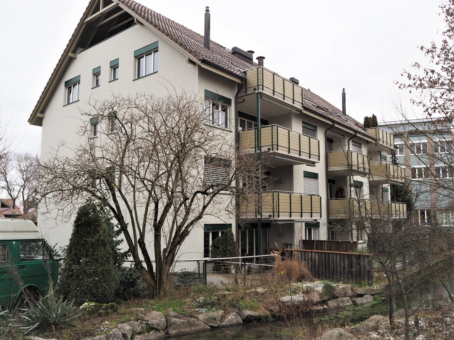 white building, balcony on the second floor, sloped roof, green trim, windows, entrance