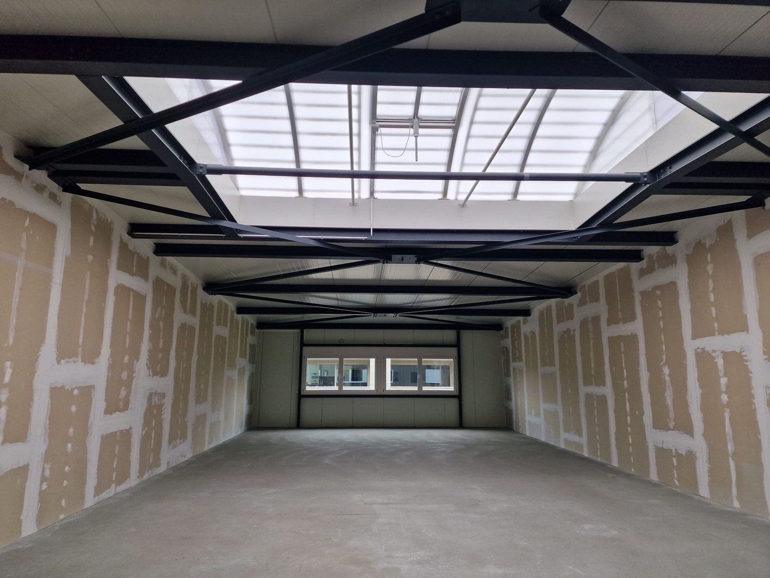 Empty room with concrete floor, unfinished walls, metal roof structure, and windows