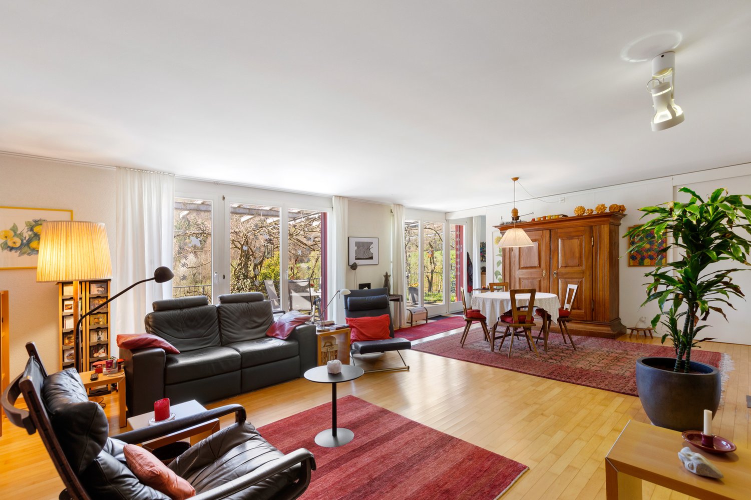 modern living room, black leather couches, wooden floor, large windows, balcony, dining table, wooden cabinet, potted plant