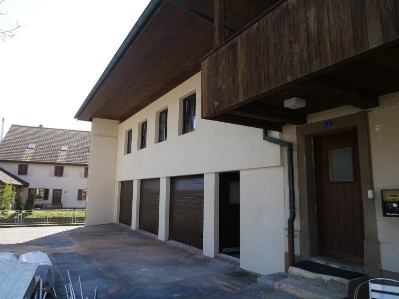 Front view of a house with white wall and brown wooden top, balcony, multiple garages in the front and a door