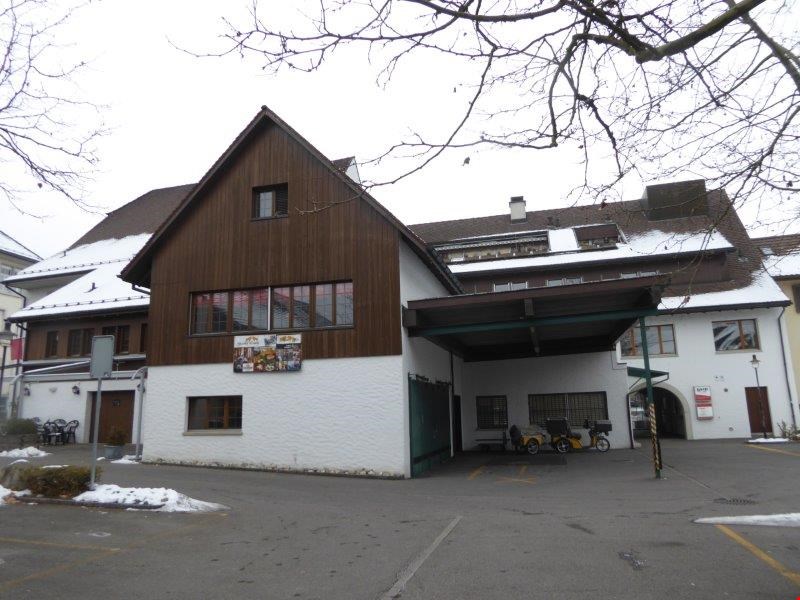 A two-story wooden and white building with a garage entrance on the ground floor. The building has a slanted roof and several windows.