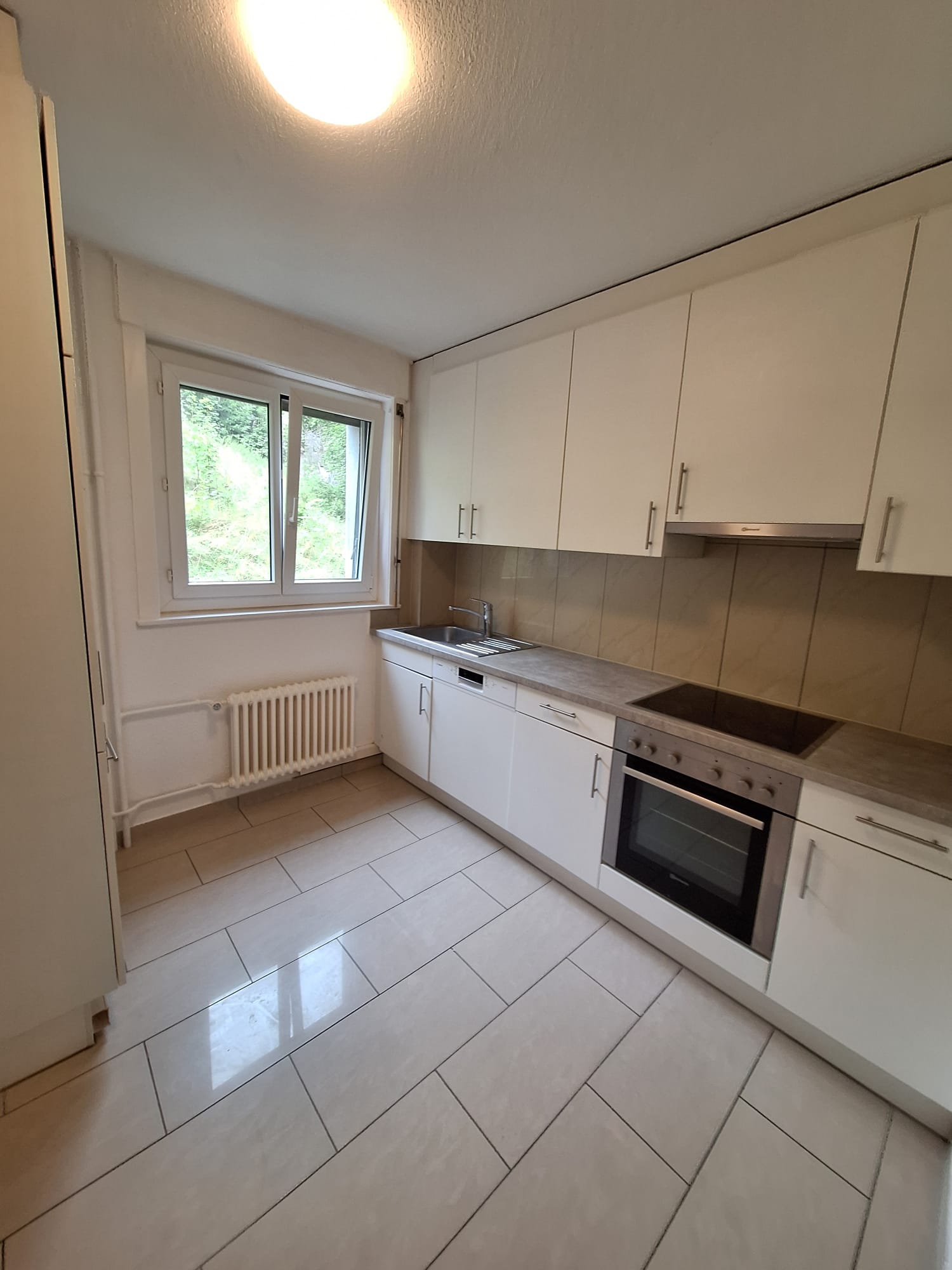 Modern kitchen with white tiled flooring, white cabinetry, stainless steel appliances, a large window with a view, under cabinet lighting, a dishwasher and a sink